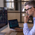 an investor reviewing graphs and charts on multiple computers