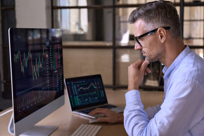 an investor reviewing graphs and charts on multiple computers