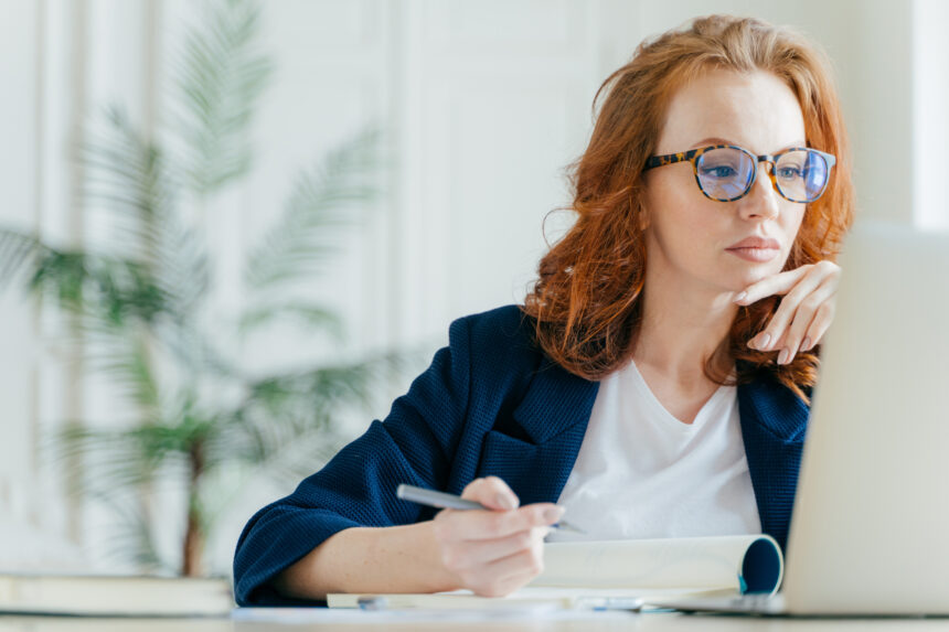 investor considers screen while writing on pad