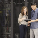 people viewing a mobile device in front of stacks of supercomputers