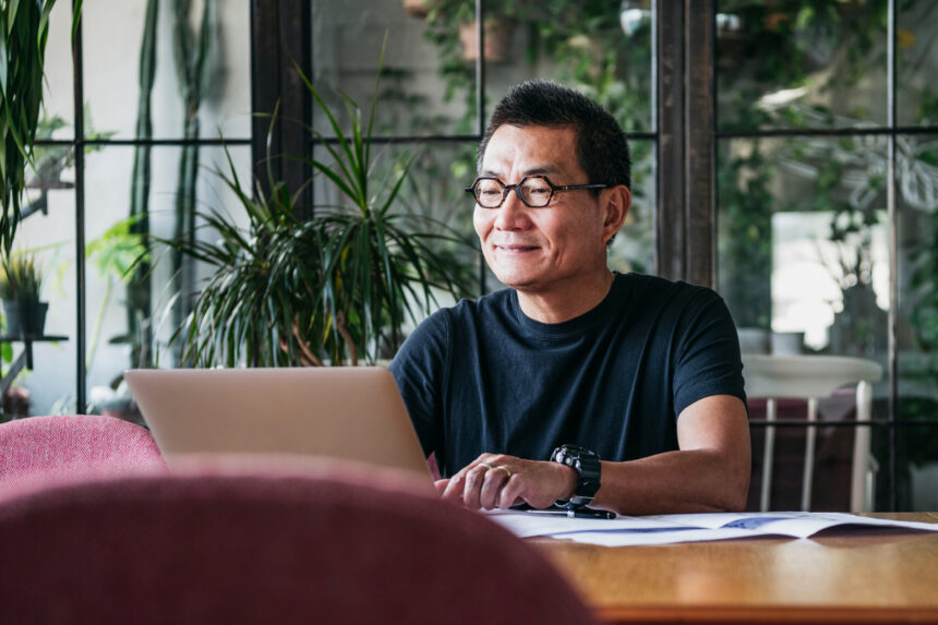 an investor smiles while sitting at a table in front of a laptop computer