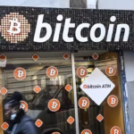 1230477979 the reflection of a woman walking past a bitcoin digital currency atm shop in marseille.j