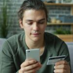 491f254fb0b5be1dd7459bfc61cdde9e8ae2a2df person using a smartphone while holding a credit card